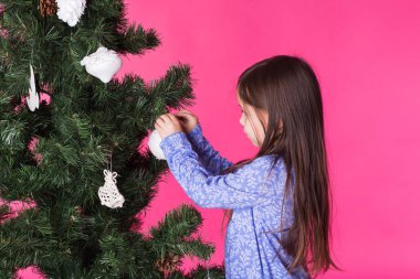 Çocuklar, tatil ve Noel kavramı - küçük kız pembe bir arka plan üzerinde Noel ağacı süsleme
