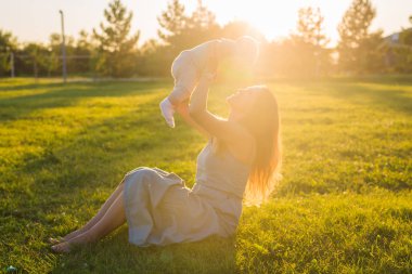Güneşli bir çayır çocuğu olan kadın. Yaz günbatımı üzerinde mutlu bir aile. Bebek annesiyle.