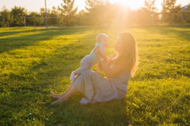 Güneşli bir çayır çocuğu olan kadın. Yaz günbatımı üzerinde mutlu bir aile. Bebek annesiyle.