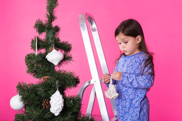 Kinder, Feiertage und Weihnachtskonzept - kleines Mädchen schmückt Weihnachtsbaum auf rosa Hintergrund — Stockfoto