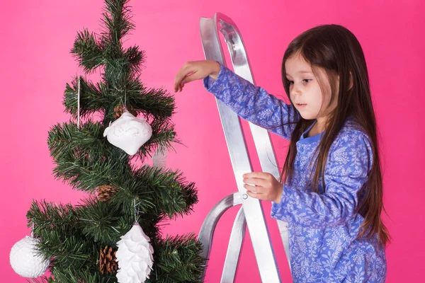 Jul och semester koncept - en liten flicka dekorera julgran på rosa bakgrund — Stockfoto