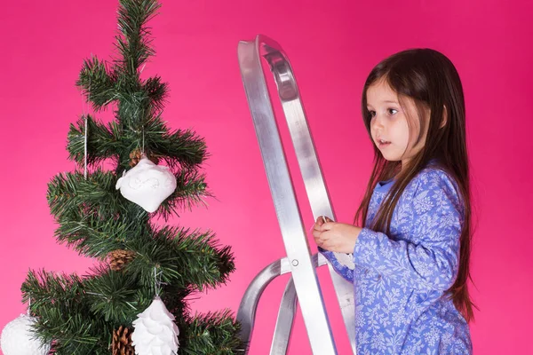 Jul och semester koncept - en liten flicka dekorera julgran på rosa bakgrund — Stockfoto