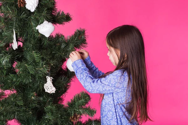 Children, holidays and christmas concept - little girl decorating christmas tree on pink background — Stock Photo, Image