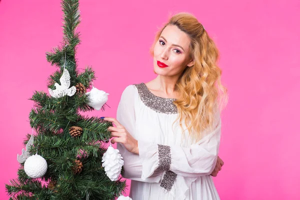Άνθρωποι, τις διακοπές και τα Χριστούγεννα έννοια - νεαρός ξανθιά γυναίκα στέκεται κοντά στο χριστουγεννιάτικο δέντρο σε ροζ φόντο — Φωτογραφία Αρχείου