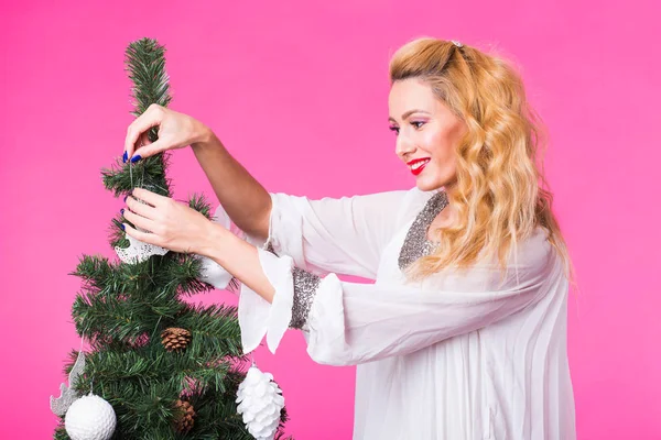 Weihnachten, Feiertage und Menschen Konzept - junge glückliche blonde Frau schmückt Weihnachtsbaum auf rosa Hintergrund — Stockfoto