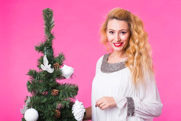 Άνθρωποι, τις διακοπές και τα Χριστούγεννα έννοια - νεαρός ξανθιά γυναίκα στέκεται κοντά στο χριστουγεννιάτικο δέντρο σε ροζ φόντο — Φωτογραφία Αρχείου