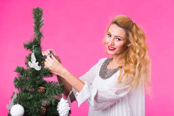 Άνθρωποι, τις διακοπές και τα Χριστούγεννα έννοια - νεαρή γυναίκα κρέμονται Χριστούγεννα μπάλα για το χριστουγεννιάτικο δέντρο στην ροζ backgroung — Φωτογραφία Αρχείου