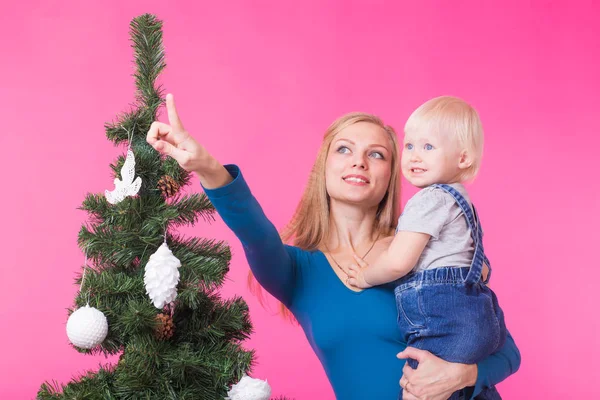 Boże Narodzenie, święta i koncepcja ludzie - młoda kobieta szczęśliwa z córką na rękach Pokaż ozdoby na choinkę — Zdjęcie stockowe