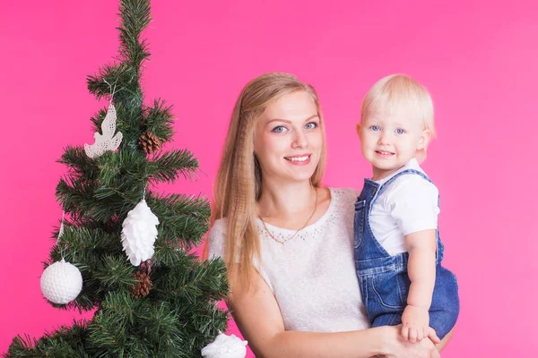 休日や人々 のコンセプト - 女性とピンク色の背景上にクリスマス ツリーの近く彼女の子供 — ストック写真