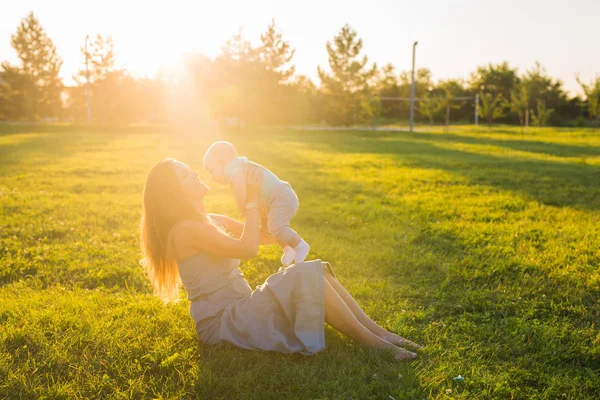 Ung kvinna med pojke på ängen på en solig dag. Lycklig familj på sommar solnedgång. Mor med baby. — Stockfoto