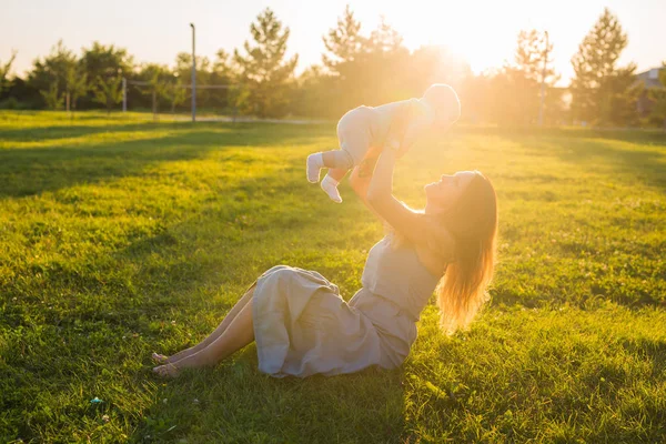 Jeune femme avec garçon dans la prairie par une journée ensoleillée. Bonne famille au coucher du soleil d'été. Mère avec bébé . — Photo