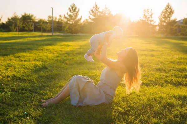Jeune femme avec garçon dans la prairie par une journée ensoleillée. Bonne famille au coucher du soleil d'été. Mère avec bébé . — Photo