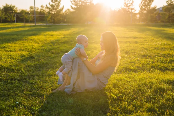 화창한 날에 풀밭에 소년과 젊은 여자. 여름 일몰에 행복 한 가족입니다. 아기와 엄마. — 스톡 사진