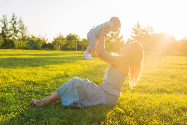 Ung kvinna med pojke på ängen på en solig dag. Lycklig familj på sommar solnedgång. Mor med baby. — Stockfoto