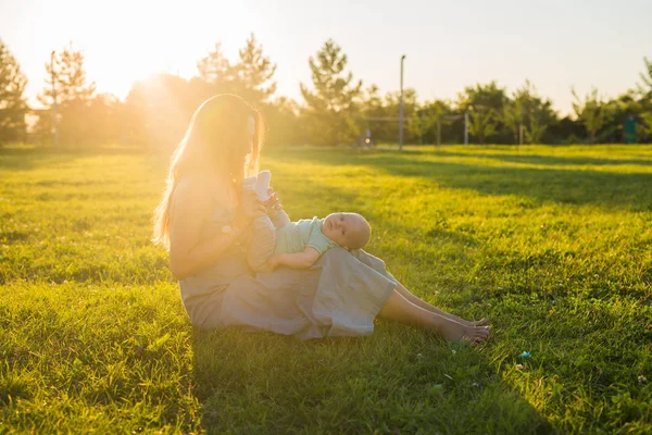 Ung kvinna med pojke på ängen på en solig dag. Lycklig familj på sommar solnedgång. Mor med baby. — Stockfoto