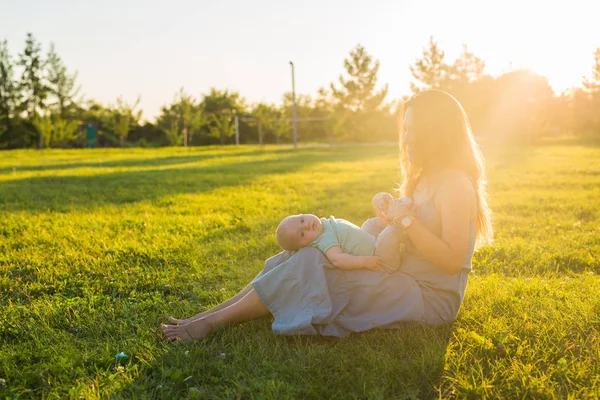 Jovem com rapaz no prado num dia ensolarado. Família feliz no pôr-do-sol de verão. Mãe com bebê . — Fotografia de Stock