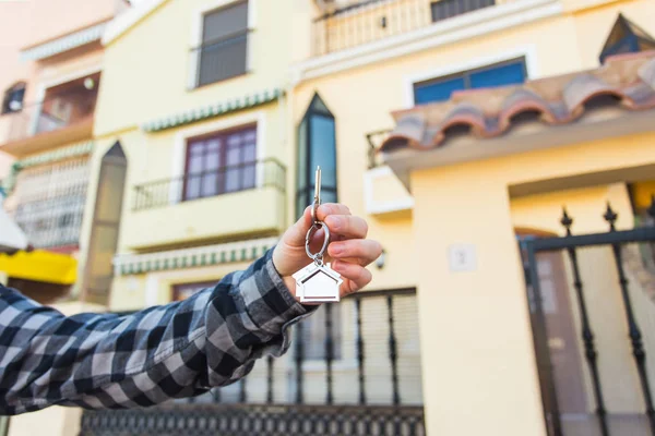 Manos sosteniendo las llaves de la casa en forma de llavero en frente de un nuevo hogar . —  Fotos de Stock