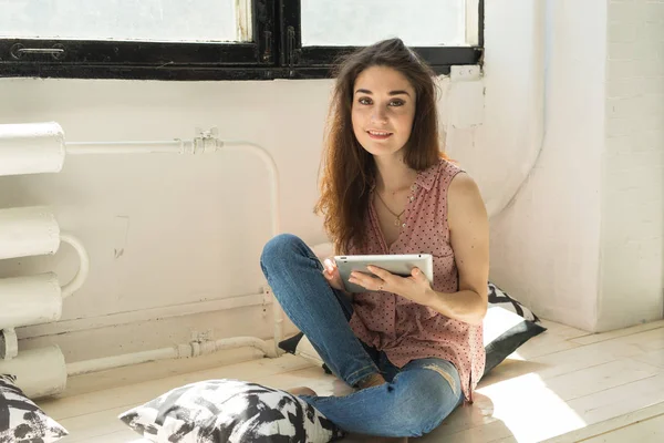 Tecnologia e concetto di persone - Giovane bella donna seduta sul davanzale di legno con tablet e cuscini — Foto Stock