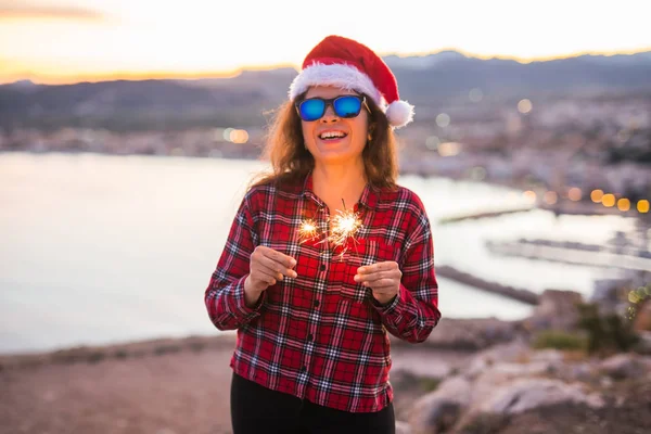 İnsanlar, güzellik ve Noel kavramı - güneş gözlüğü ve santa claus şapka sparkles tutan güzel kadın