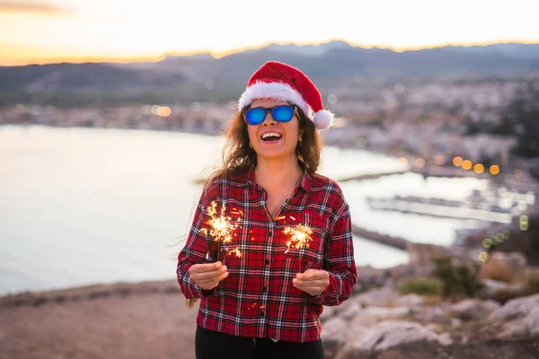 İnsanlar, güzellik ve Noel kavramı - güneş gözlüğü ve santa claus şapka sparkles tutan güzel kadın