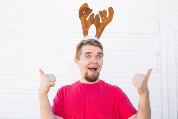 Tatil ve Noel kavramı - geyikler boynuzları jest beyaz zemin üzerine başparmak ile genç adam — Stok fotoğraf