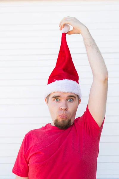 Vacaciones, Navidad y concepto de ropa - sorprendido hombre guapo divertido en sombrero de santa posando sobre fondo blanco — Foto de Stock