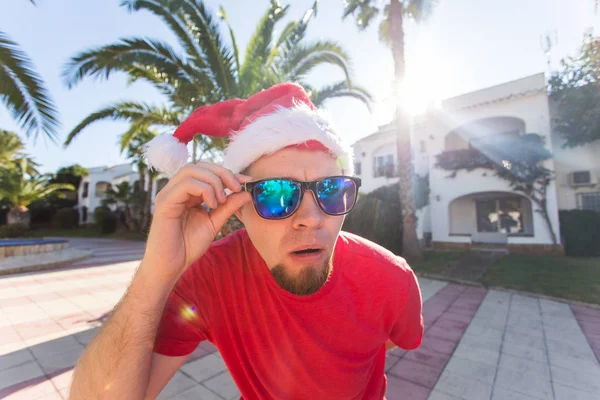 Şaka, tatil ve Noel kavramı - santa şapka güneş gözlüğü tutan genç komik neşeli adam