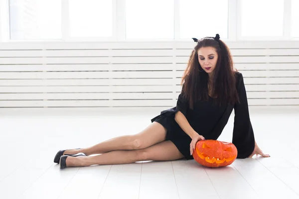 Upphetsad glad ung kvinna i Halloweenkostym poserar med snidade pumpa i lightroom — Stockfoto