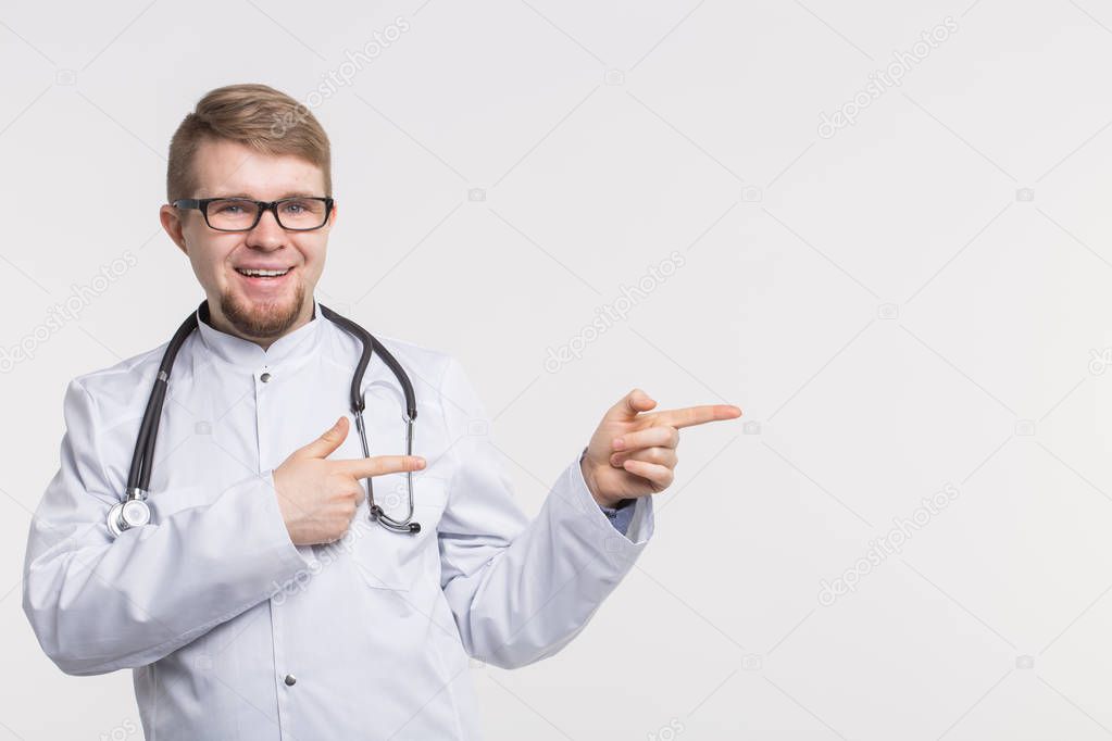 Portrait of happy young doctor in studio with stethoscope pointing right