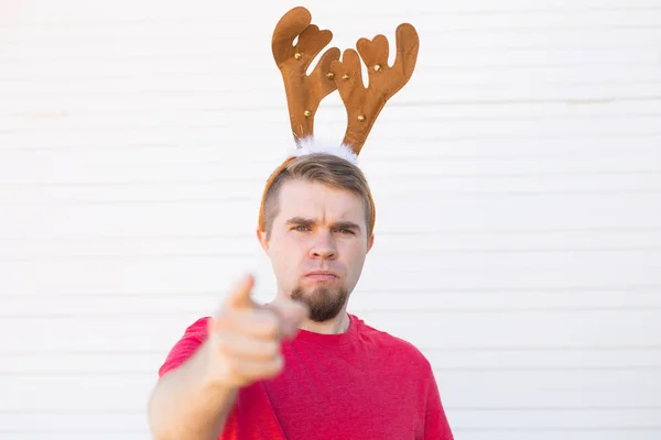 Navidad, gente, concepto de emociones - hombre enojado insatisfecho en cuernos de venado de Navidad señalando al espectador — Foto de Stock
