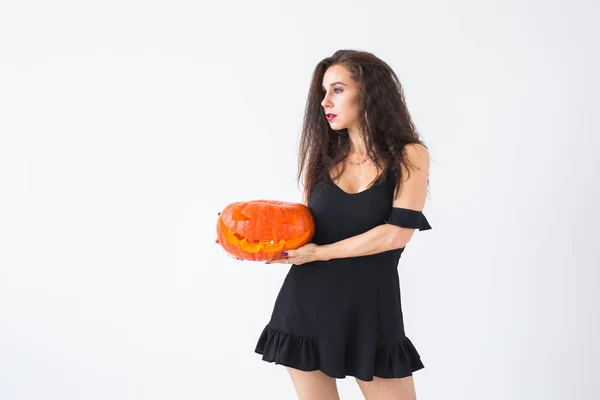 Cute gothic woman in halloween style clothes with pumpkin in hands over light background with copy space — Stock Photo, Image