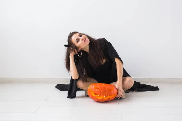 Улыбающаяся брюнетка в макияже на Хэллоуин позирует с резной тыквой — стоковое фото