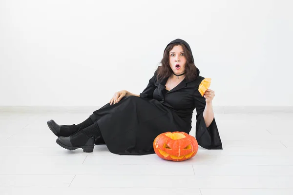 Surprised young woman in halloween costume posing with carved pumpkin in lightroom — Stock Photo, Image