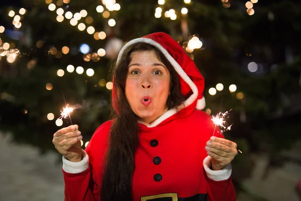 Urlaub, Weihnachten und Menschen-Konzept - junge glückliche Frau im Weihnachtsanzug hält Bengalisches Licht über den Christbaumhintergrund — Stockfoto