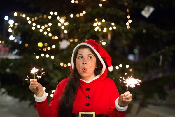 Tatil, mutluluk, kavram - genç kadın elleri ışıkları ile Noel ağacı yakınındaki gülümseyen Noel kıyafetli insanlar — Stok fotoğraf