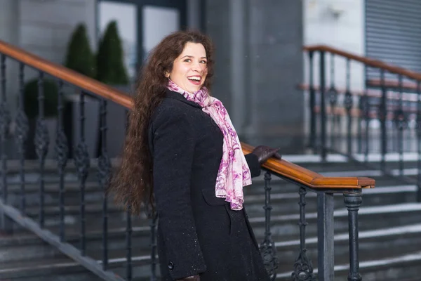 Stad en mensen concept - mooi en gelukkig vrouw in zwarte jas en sjaal roze staande op de trap — Stockfoto