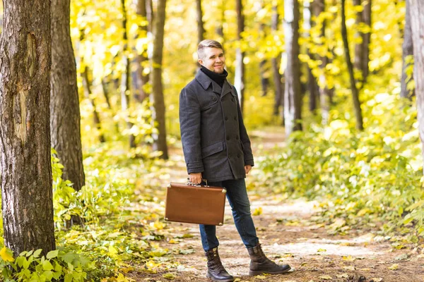 Sonbahar, mevsim ve insanlar kavramı - Sonbahar Park retro çanta ile ayakta yakışıklı adam