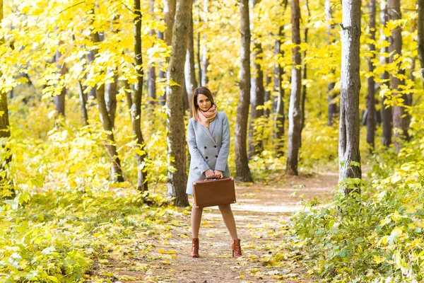 Fall, season and people concept - young woman standing with retro suitcase in autumn park — Stock Photo, Image