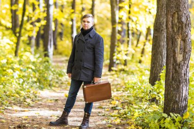 Sonbahar, mevsim ve insanlar kavramı - Sonbahar Park retro çanta ile ayakta yakışıklı adam