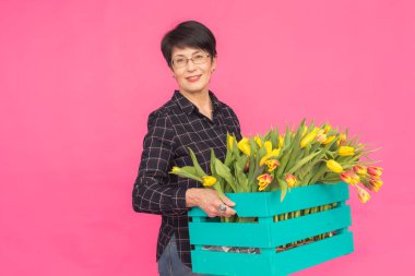 Mutlu güzel esmer beyaz orta yaşlı bir kadın ile lale pembe bir arka plan üzerinde büyük kutu.