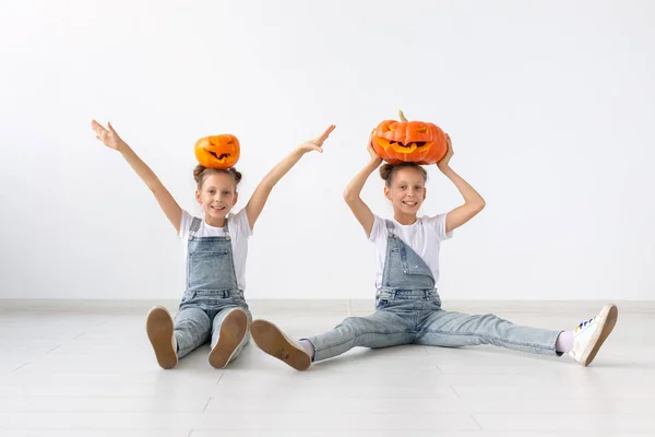 Cadılar Bayramı, çocuk ve eğlence kavramı - jack-o-lantern beyaz zemin üzerine başlarına ayakta mutlu neşeli ikiz kız kardeşler — Stok fotoğraf