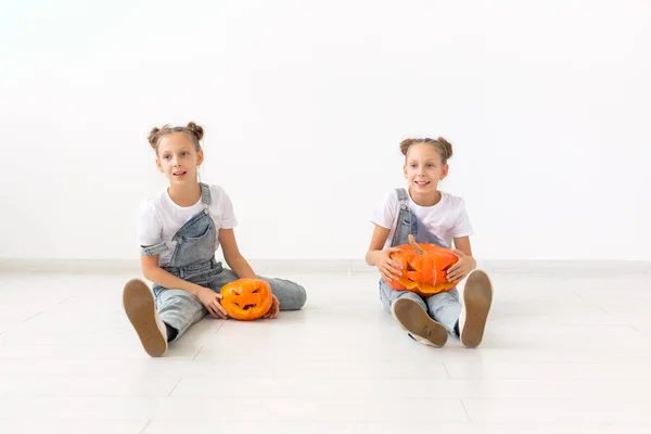 Halloween, bambini e concetto di infanzia - Sorelle gemelle allegre felici sedute con zucche jack-o-lanterna su sfondo bianco — Foto Stock