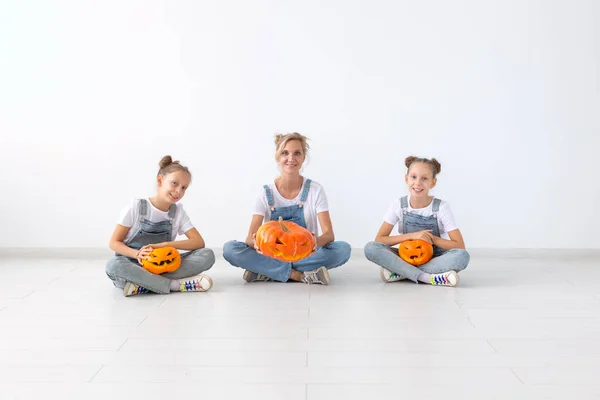 Famiglia, autunno e vacanze concetto - Madre e le sue figlie gemelle che tengono Jack-O-Lanterna zucca il giorno di Halloween . — Foto Stock