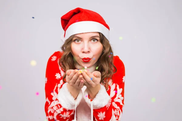 Navidad, concepto de la gente - mujer en traje de santa soplando lentejuelas de colores en el fondo con espacio de copia — Foto de Stock