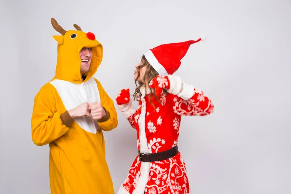 Férias, Natal e conceito divertido - Casal engraçado em traje de veado e roupas de Papai Noel estão dançando em fundo branco — Fotografia de Stock