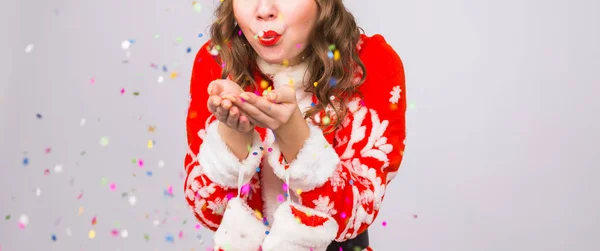 Navidad, concepto de la gente - mujer en traje de santa soplando lentejuelas de colores en el fondo con espacio de copia — Foto de Stock