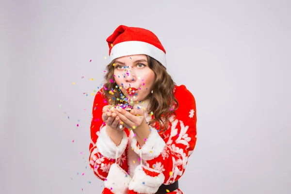 Urlaub, Weihnachten und Menschen-Konzept - schöne junge Frau im Weihnachtsmann-Kostüm über weißem Hintergrund, der Konfetti bläst — Stockfoto