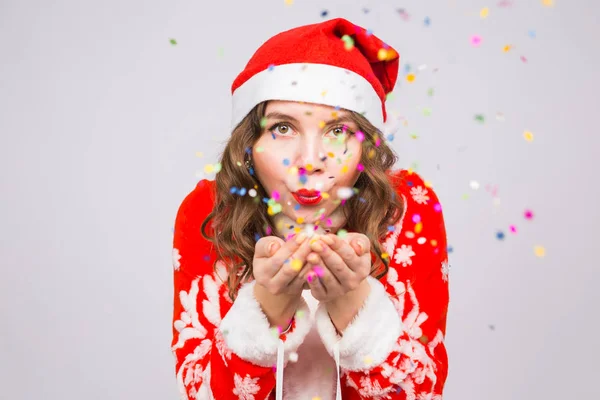 Weihnachten, Menschen Konzept - Frau im Weihnachtsanzug pustet bunte Pailletten auf Hintergrund mit Kopierraum — Stockfoto