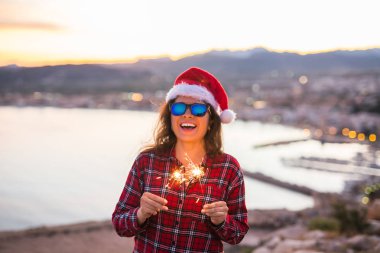 Tatil, Noel ve insanlar kavramı - Noel Baba şapkası havai fişek ve havai fişekleri ile güzel manzara üzerinde genç mutlu kadın