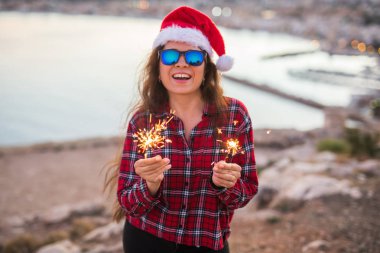 Tatil, Noel ve insanlar kavramı - Noel Baba şapkası havai fişek ve havai fişekleri ile güzel manzara üzerinde genç mutlu kadın